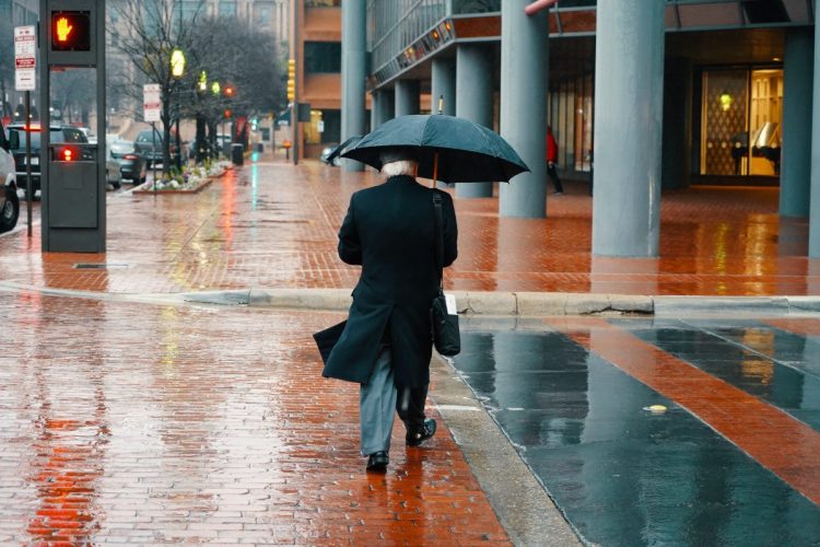 A distinguished professional approaching retirement walks to work in the rain.