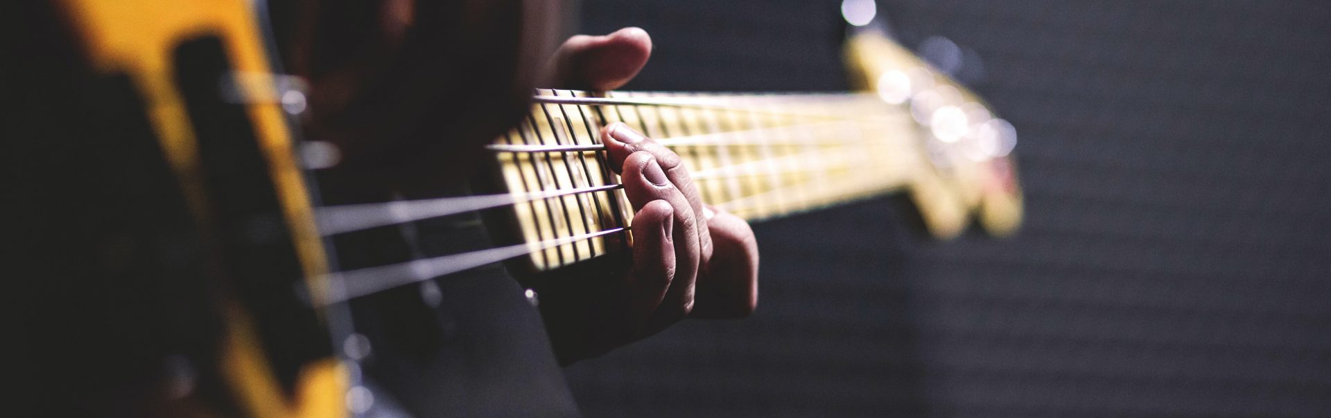 A selective focus image of a person practicing on a bass guitar.