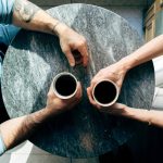 an overhead shot of two people getting coffee on a round wooden table