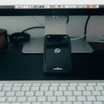 A mobile phone operating WhatsApp sits on a desk with a computer.