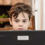 A young student works in front of a laptop. A recent survey indicates that parents and teachers disagree over the benefits of online learning.