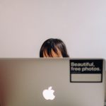 A small child sits with their face obscured by a computer on their lap.