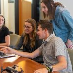 A work team gathers around a laptop