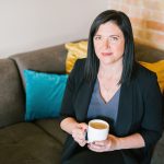 A woman sits on a couch holding a cup of coffee.