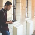 a student using technology checks his phone leaning against a wall