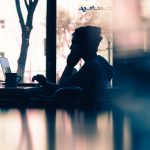 A learner in silhouette works at his laptop at a desk.