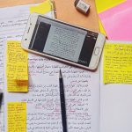 Notes and a mobile device containing arabic script sit on a desk.