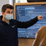 A teacher uses a smart board displaying code