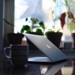 A laptop stands partway open on a table in a shadowy living room.