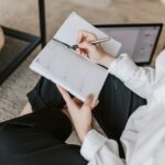 Woman writing in her planner with laptop next to her.