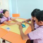 Three children from the workshop working on a machine on a table.