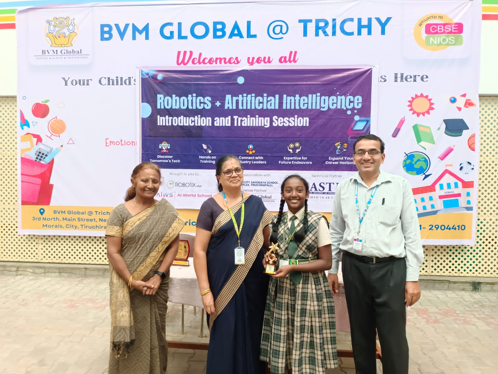 Photograph of the envent, with three teachers and a student holding a prize. 