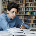 Serious high school pupil working on graduation project in library