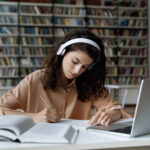 Serious busy hardworking student girl in headphones working essay