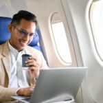 Smart Asian businessman sipping coffee, using a laptop to manage his tasks during the flight.