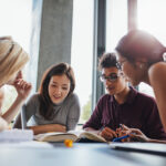 Group of young people sitting at table reading books